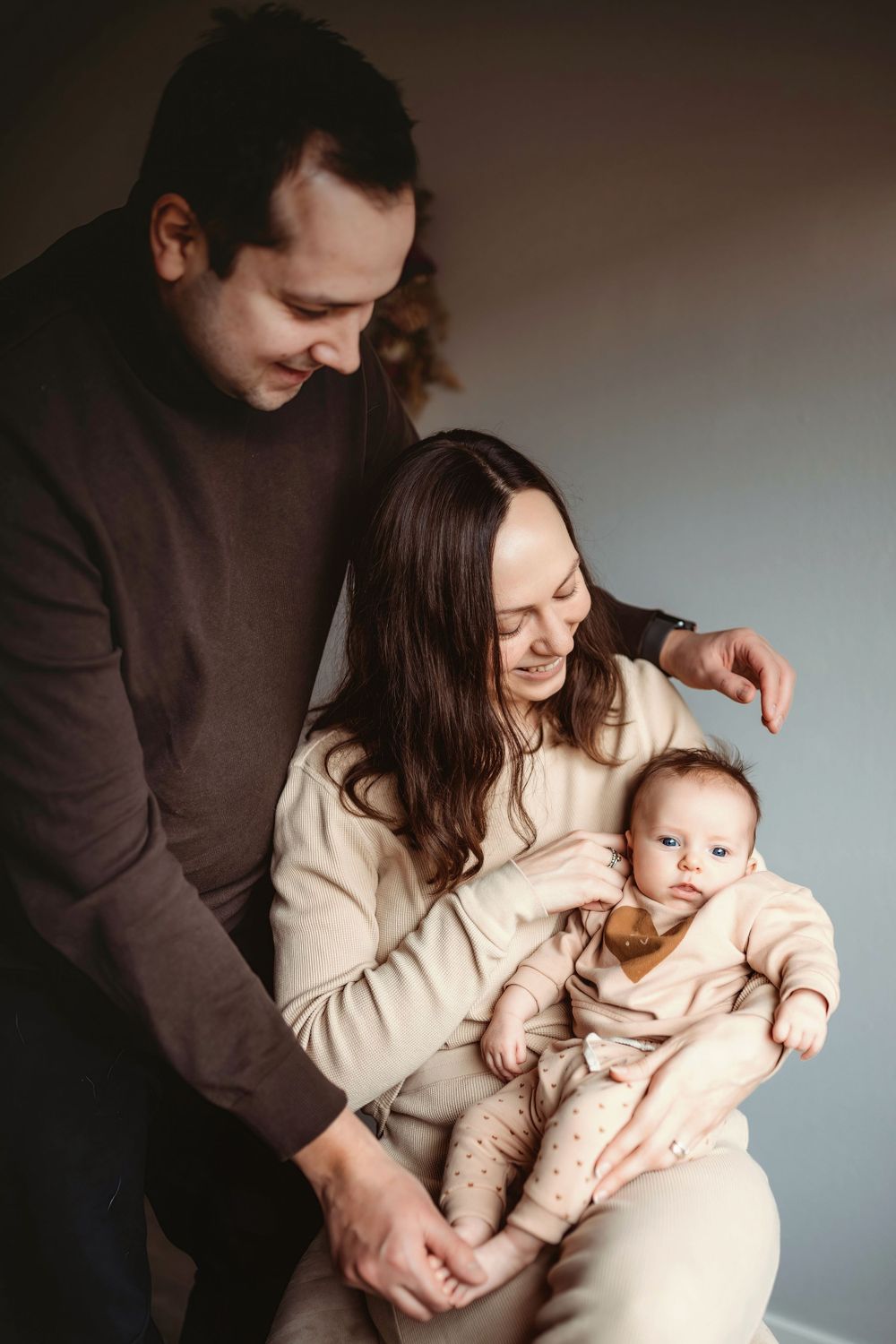 Family portrait in warm tones showing intimate moment with baby in beige outfits.