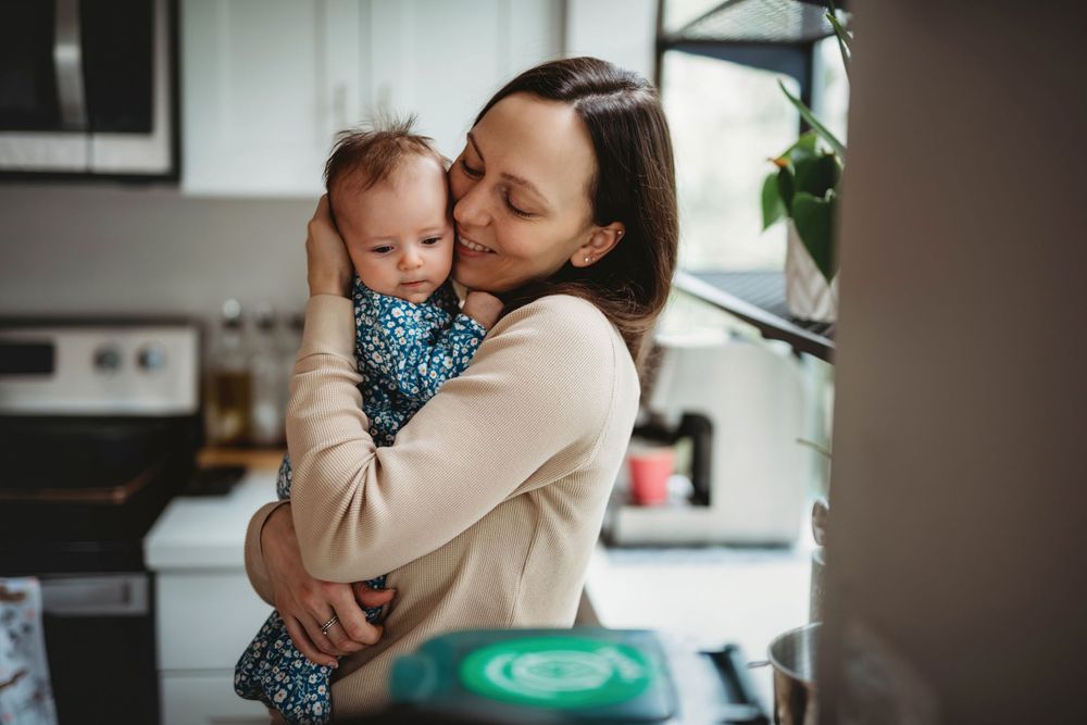A tender moment between parent and infant in a sunny kitchen setting.
