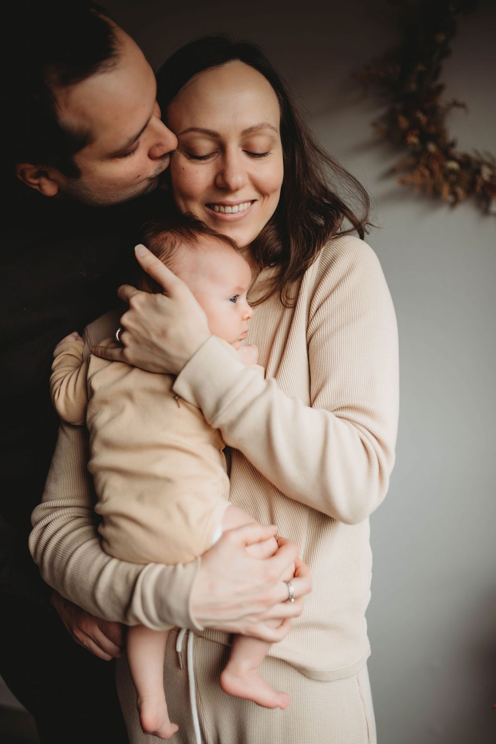 Intimate family portrait in warm neutral tones showing affectionate moment with baby.