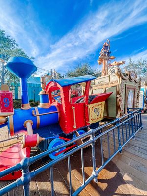 A colorful vintage-style amusement park train with red and blue cars under bright blue skies at a theme park.