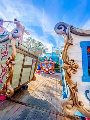 Decorative wooden railings with swirling designs line a blue-painted wooden boardwalk on a sunny day.