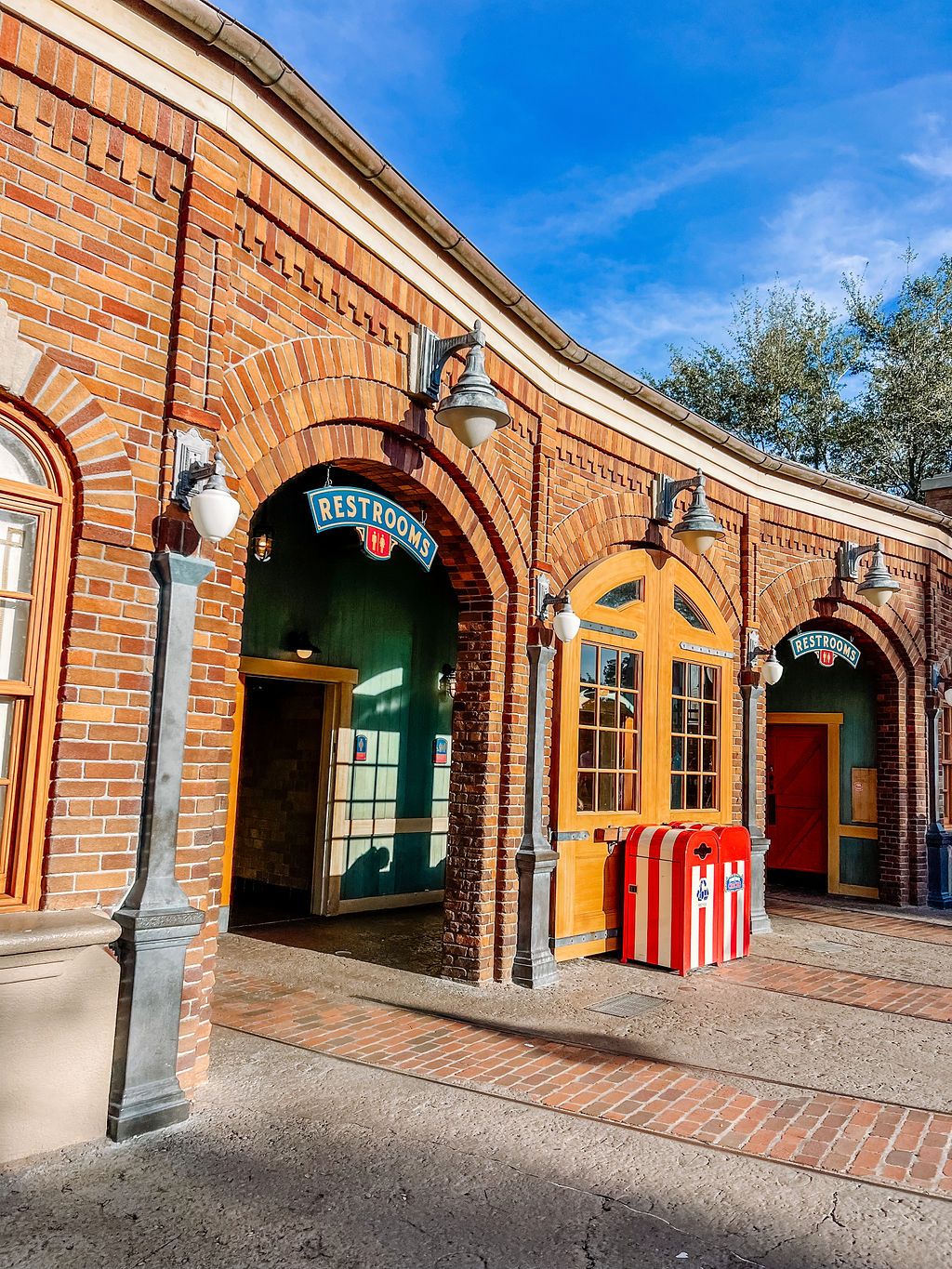 Historic red brick archways with colorful storefront windows and doors line a curved walkway under bright blue sky.