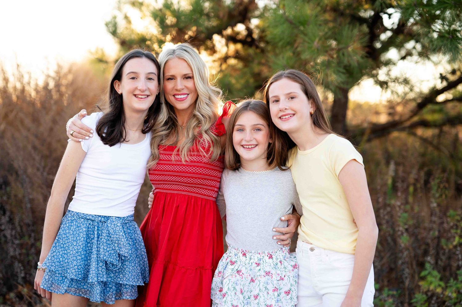 A group poses together in a meadow at sunset wearing colorful summer dresses.
