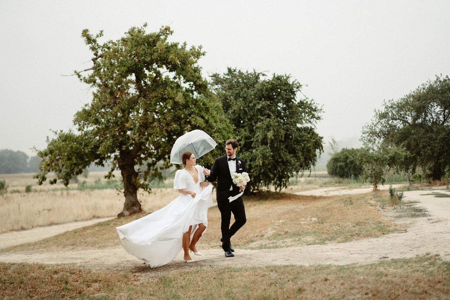 Wedding party stands on a dirt path surrounded by lush greenery and trees on an overcast day.