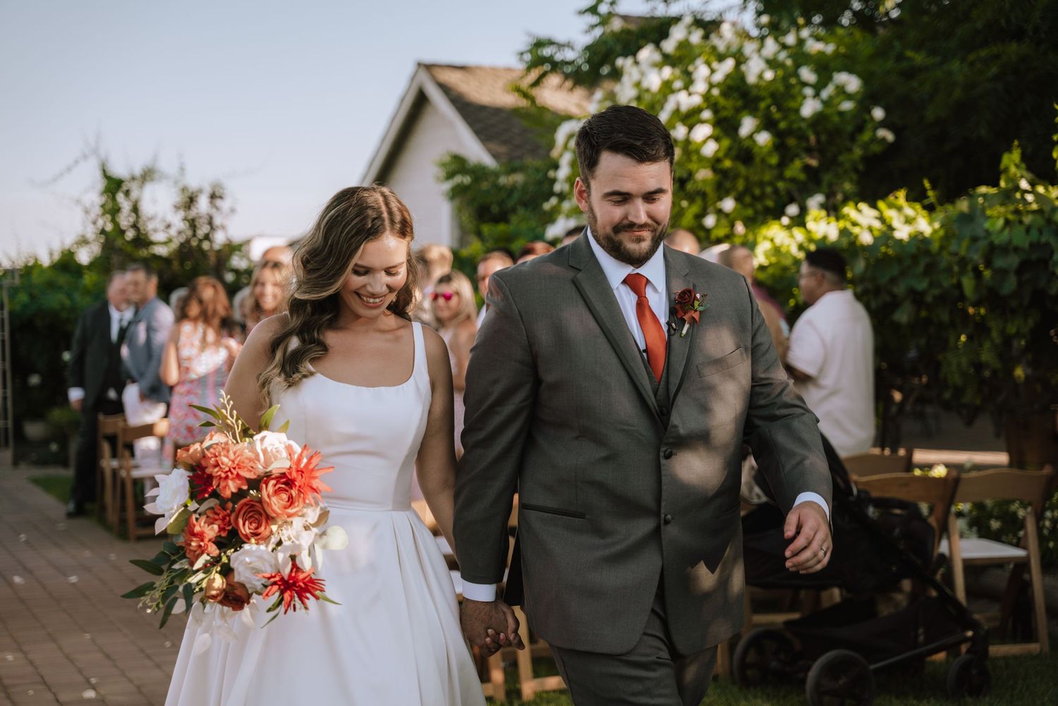 A joyful wedding celebration outdoors with warm sunset lighting as newlyweds walk together among guests.