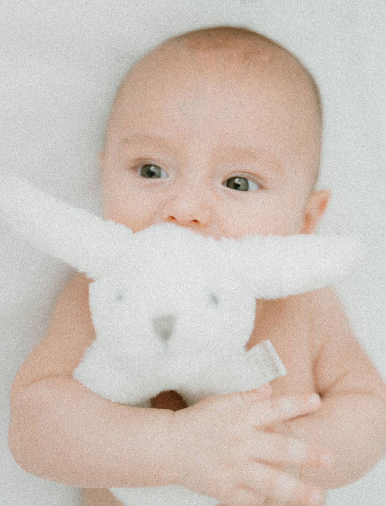 A baby hugging a white plush bunny stuffed animal against a light background.