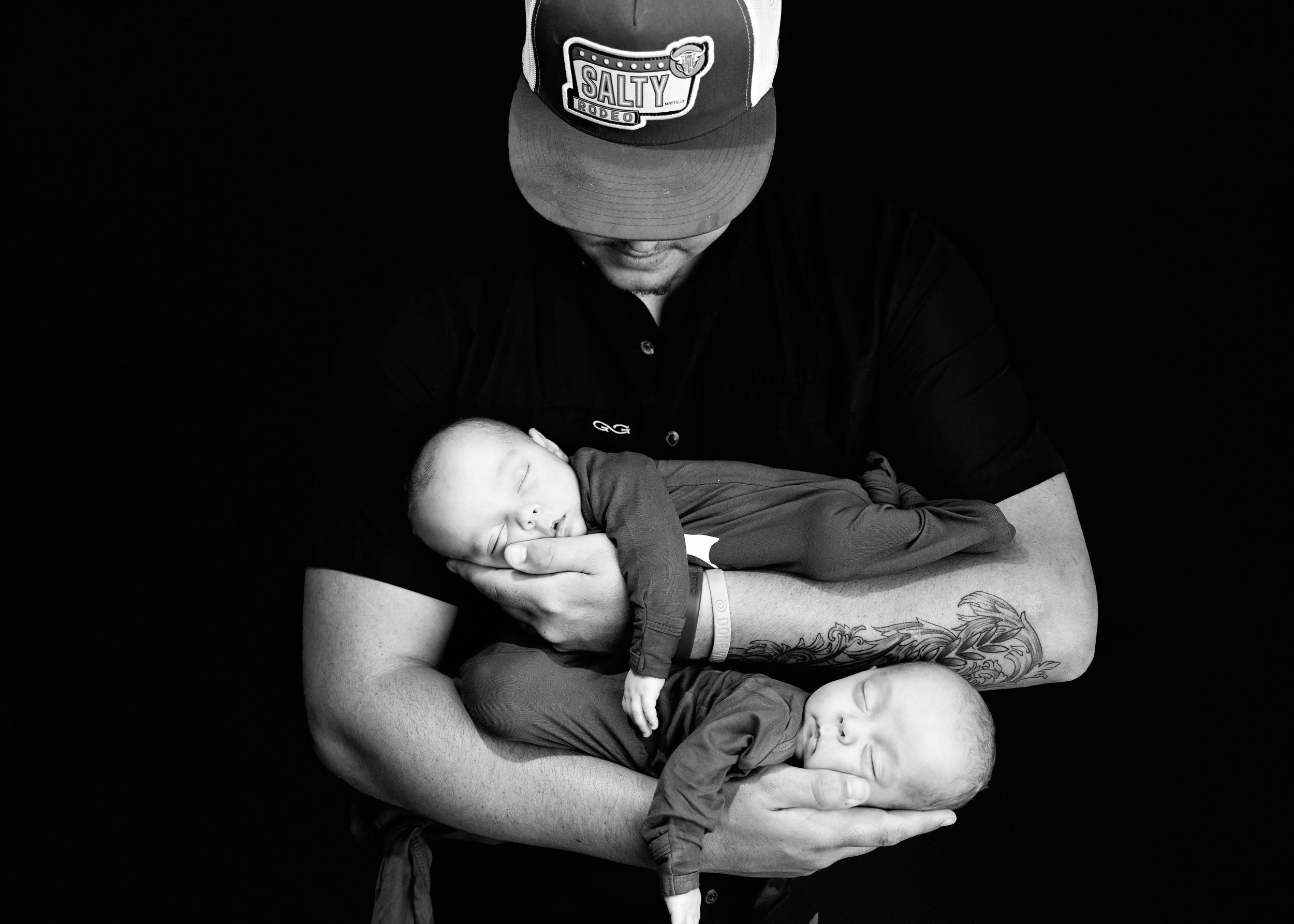 Monochrome photo shows a baby sleeping peacefully while being cradled in arms adorned with tattoos.#RoswellNM #TwinNewbornPhotographer