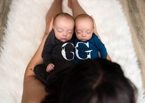 Twin newborns wearing matching dark and light colored outfits lay peacefully sleeping on soft white fur. #RoswellNM #TwinNewbornPhotographer