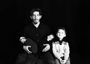 Black and white photo of dad with Twin Newborns and an older child against a black background#CarlsbadNM #NewbornPhotographer #Twins #Roswel