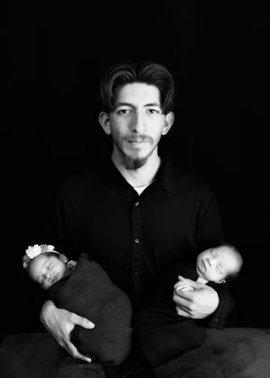 Black and white portrait of a dad in dark clothing holding two sleeping infants. #CarlsbadNM #NewbornPhotographer #Twins #RoswellNM #Artesia