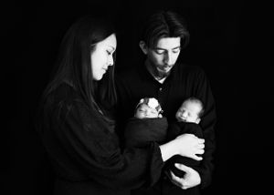 A couple dressed in black holding two babies that cast a glowing light on their faces in the darkness #TwinNewbornSession #NM