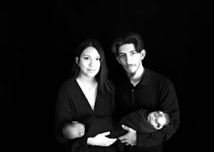 Black and white portrait of two people wearing dark clothing posing together while holding babie#TwinNewbornSession #TwinNewbornphotographer