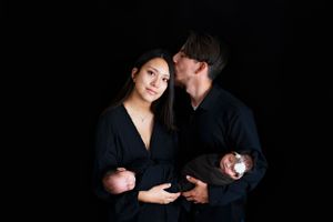 Two people in black outfits pose together against a dark background in an intimate portrait. #TwinNewbornSession #TwinNewbornphotographer