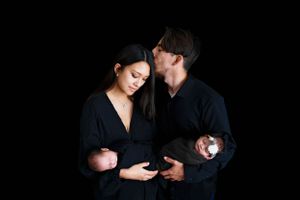 Two people wearing black clothing hold newborn twins while intimately posing against dark background#TwinNewbornSession #TwinNewbornphotogra