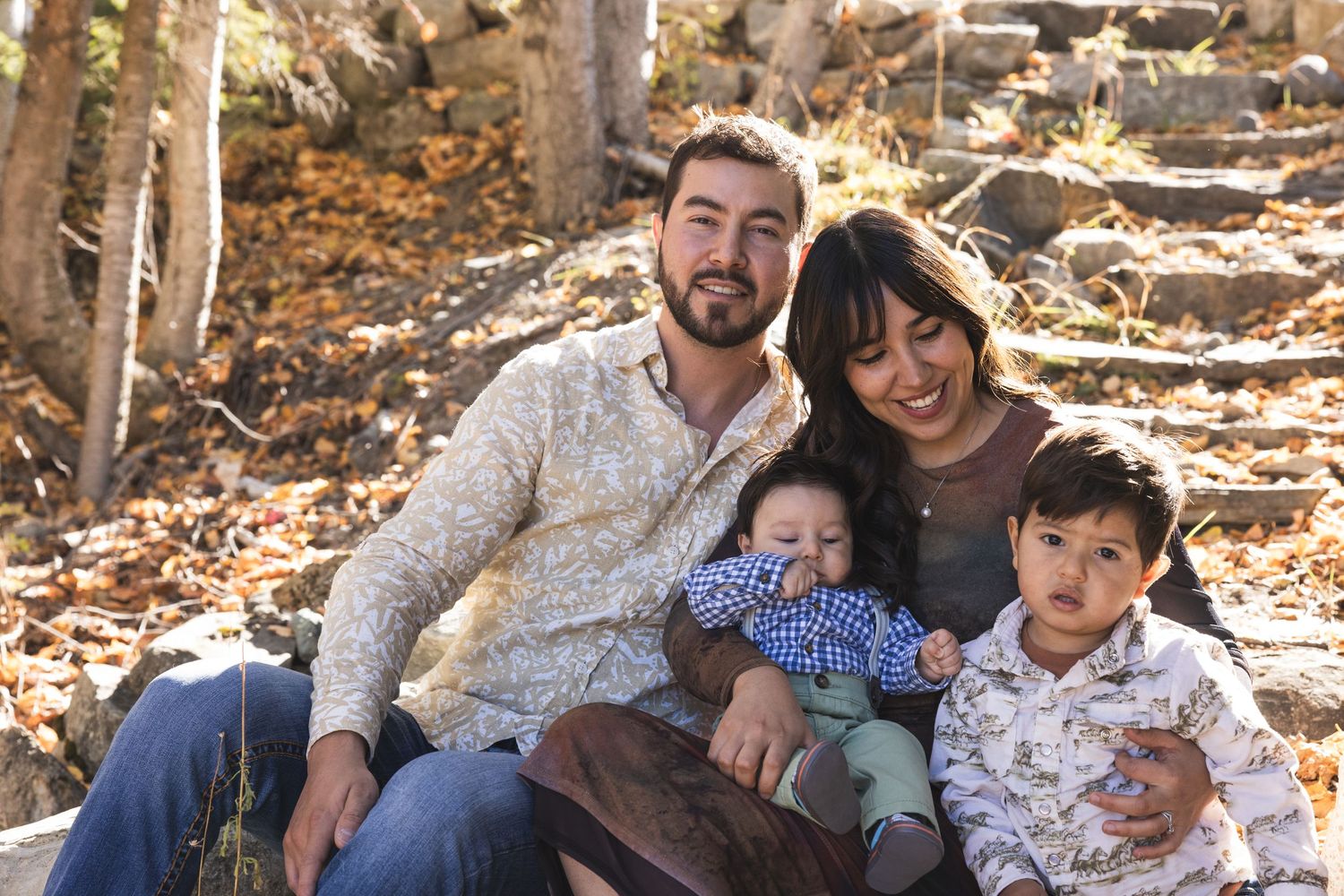 Happy family of four with two young children sitting together outdoors among autumn leaves.