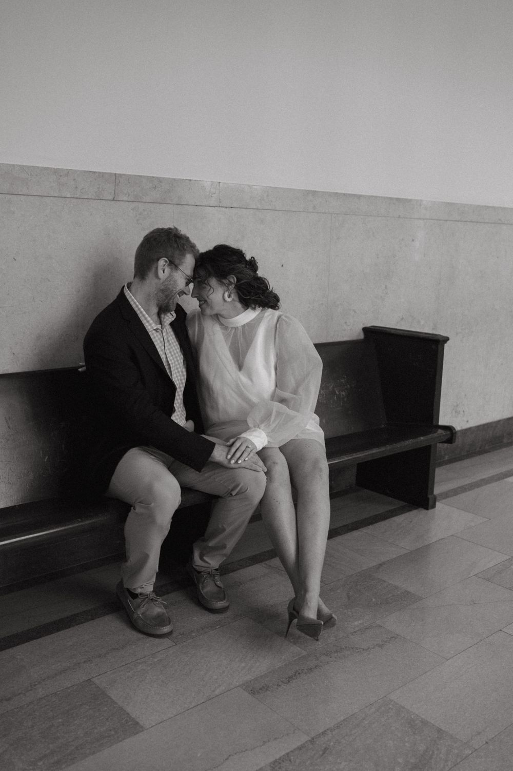 A couple sharing an intimate moment while sitting on a bench in a hallway.