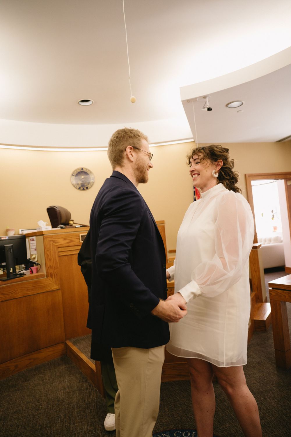 A couple shares an intimate moment in a casual office setting, wearing formal and casual attire.