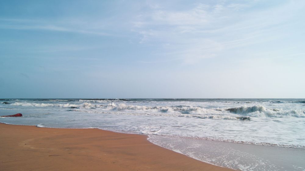 Panoramic seascape showing sandy beach and rolling waves under blue sky.