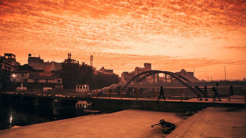 Dramatic orange sunset sky over harbor with bridge silhouette and urban buildings.