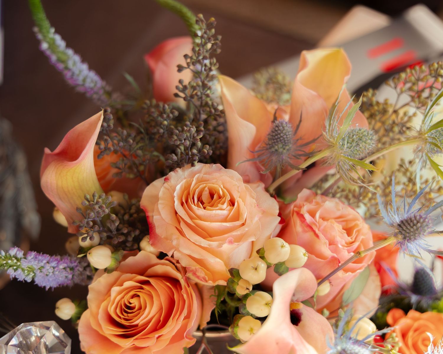 Elegant floral arrangement featuring peach roses and delicate greenery on a dark background.