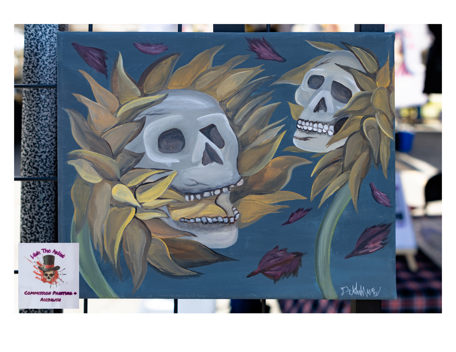 Artistic graffiti mural featuring two grey skulls with blonde hair surrounded by falling leaves and blue accents.