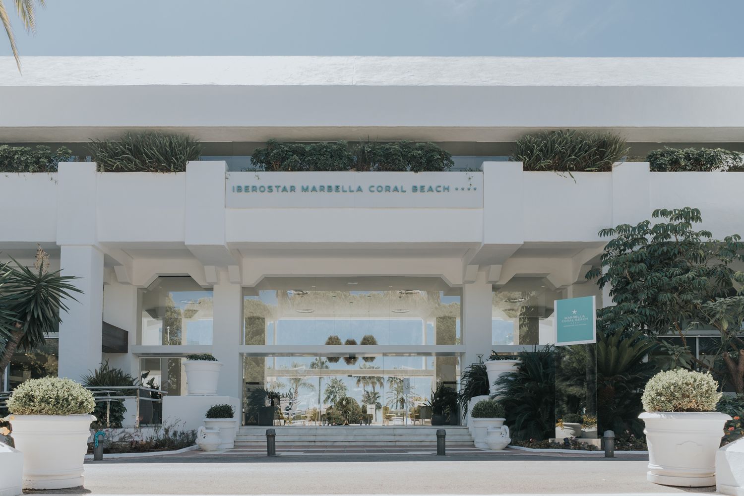 Modern white hotel entrance with archways and tropical landscaping at a beachfront resort property.
