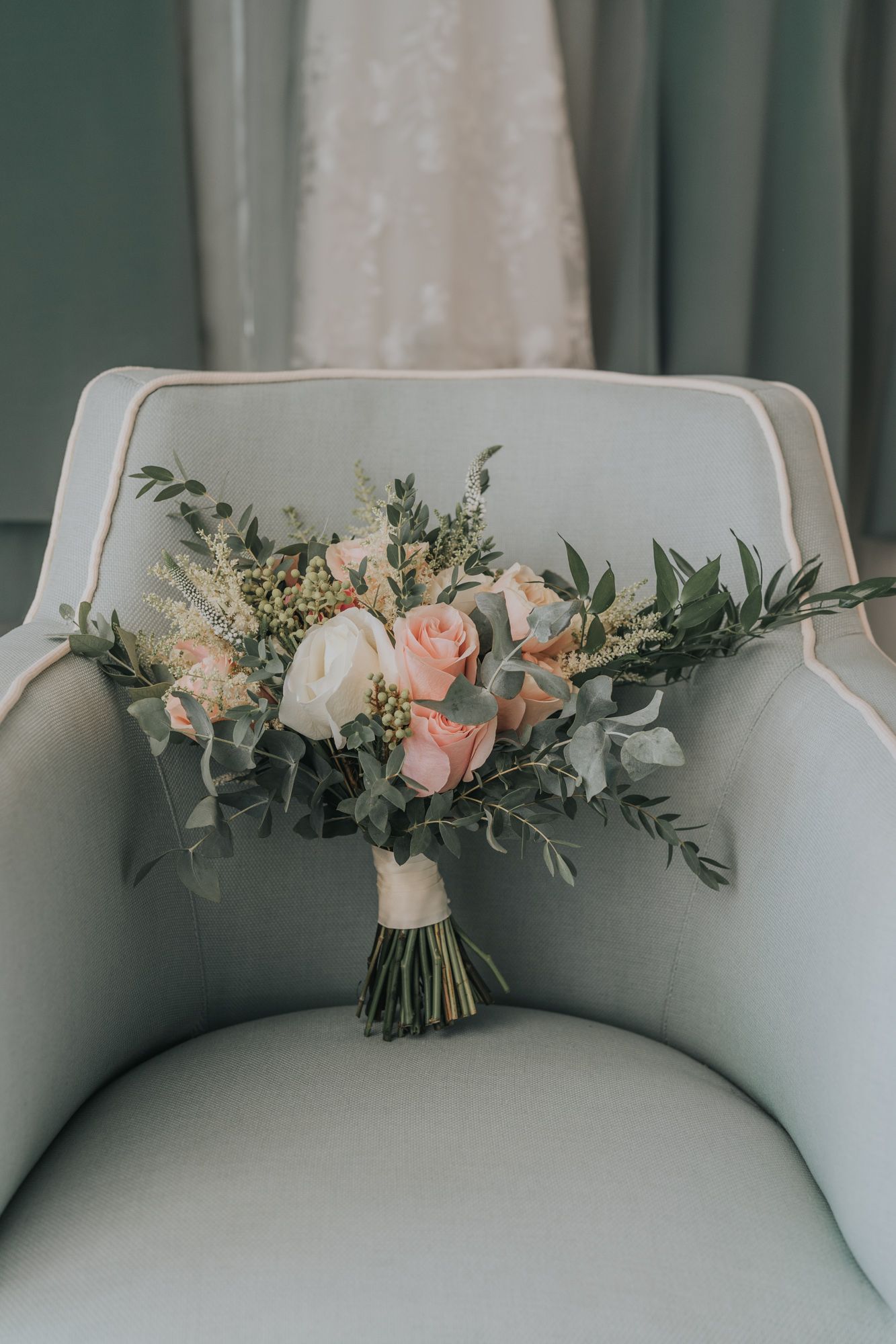 Romantic bridal bouquet with blush roses and eucalyptus greenery resting on a light gray armchair.