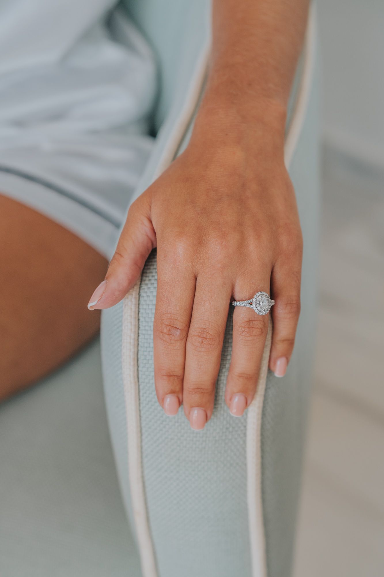 Close-up of a woman's hand wearing a sparkling round diamond engagement ring on a light blue background.