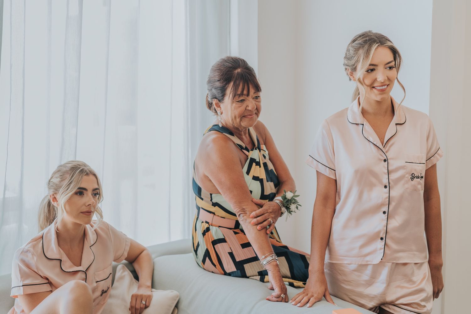 Three women in matching silk pajamas getting ready in a bright room.