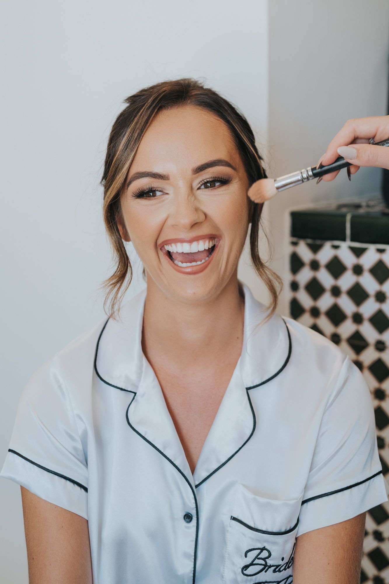 A joyful moment captured during bridal makeup preparation in a white robe.