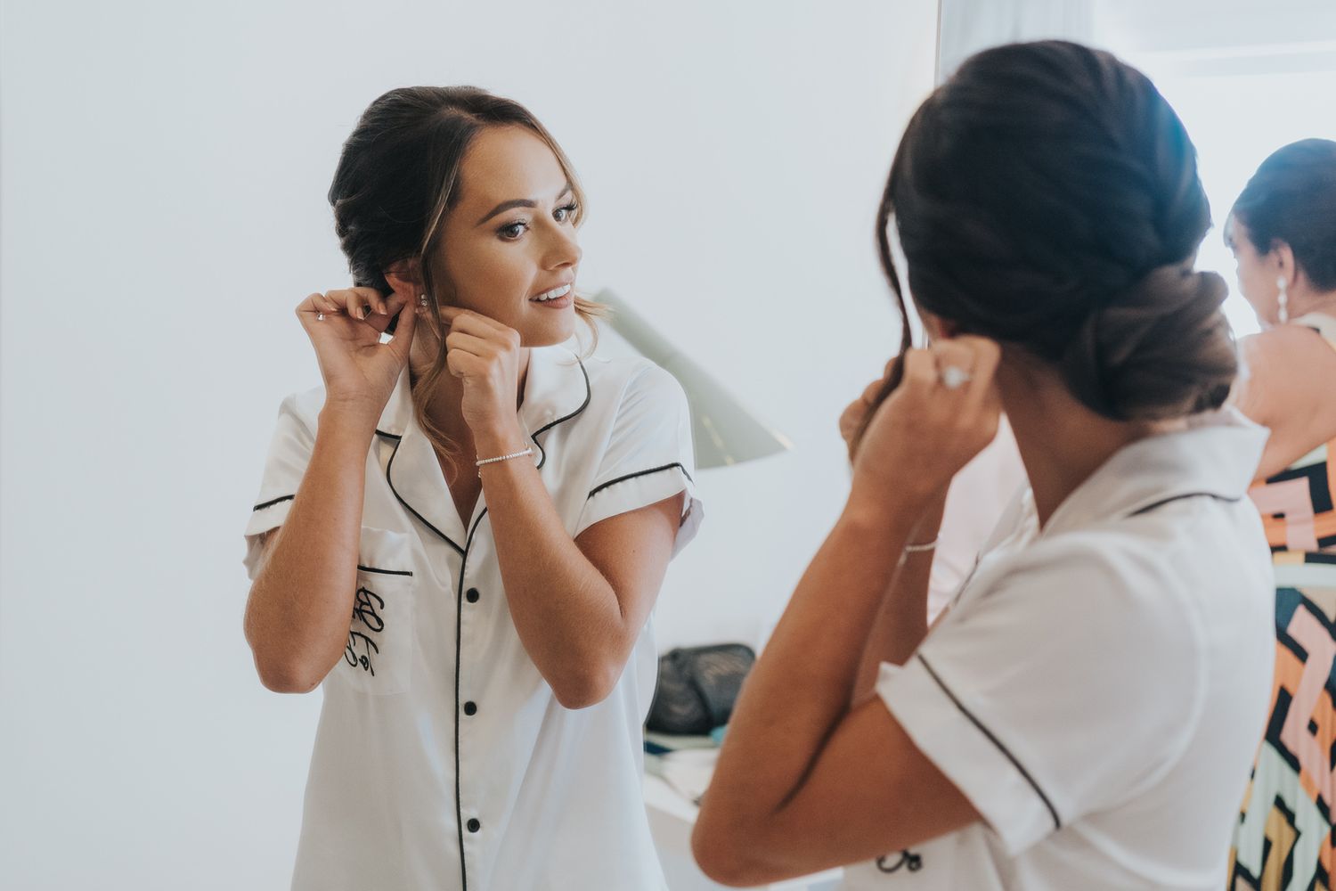 Person putting on earrings while looking in a mirror during wedding preparations.