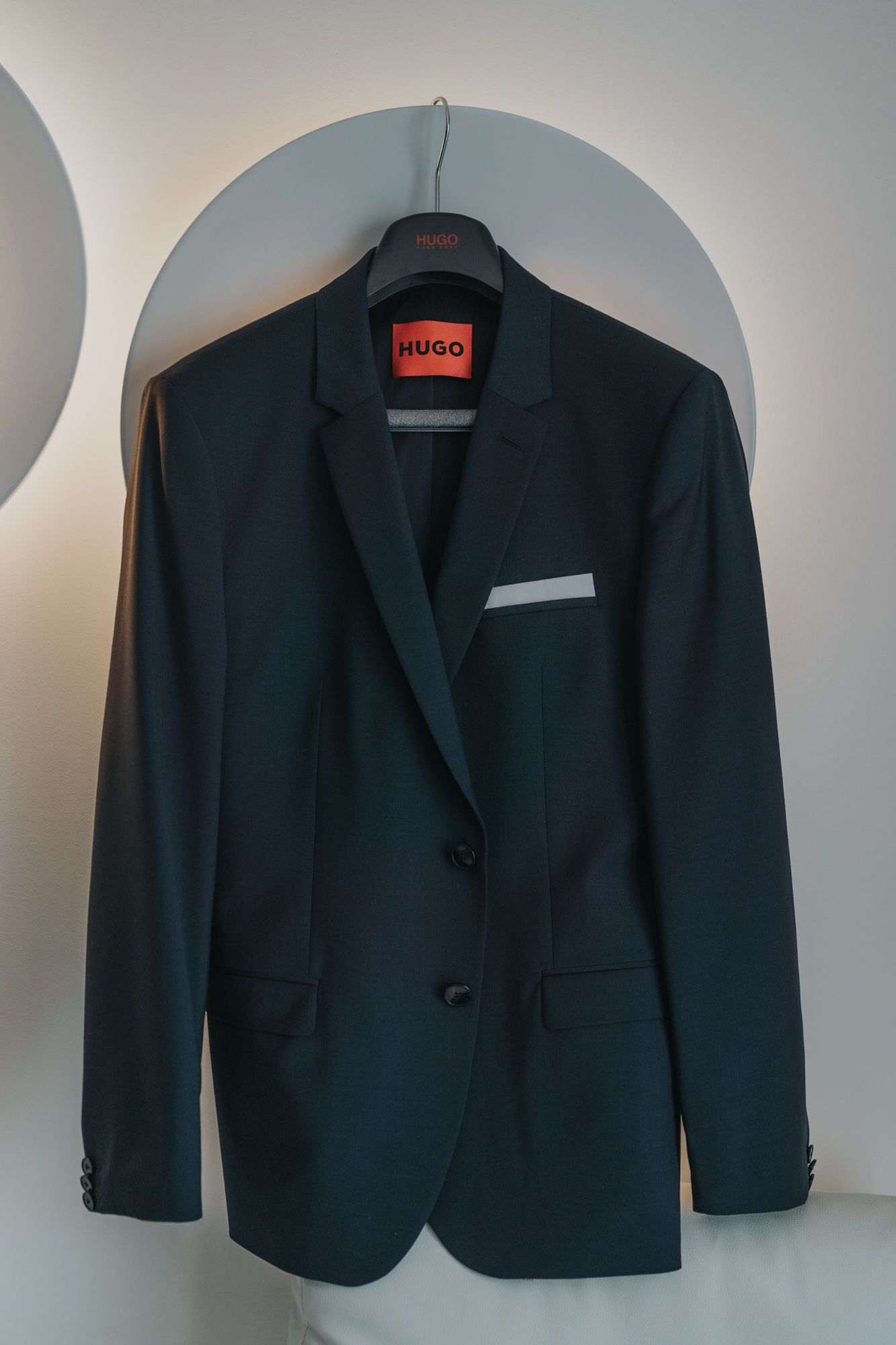 Navy blue Hugo brand suit jacket hanging on display against a white wall.