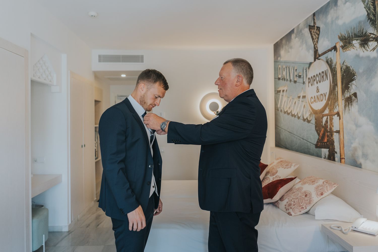 Final tie adjustments being made in hotel room before wedding ceremony.