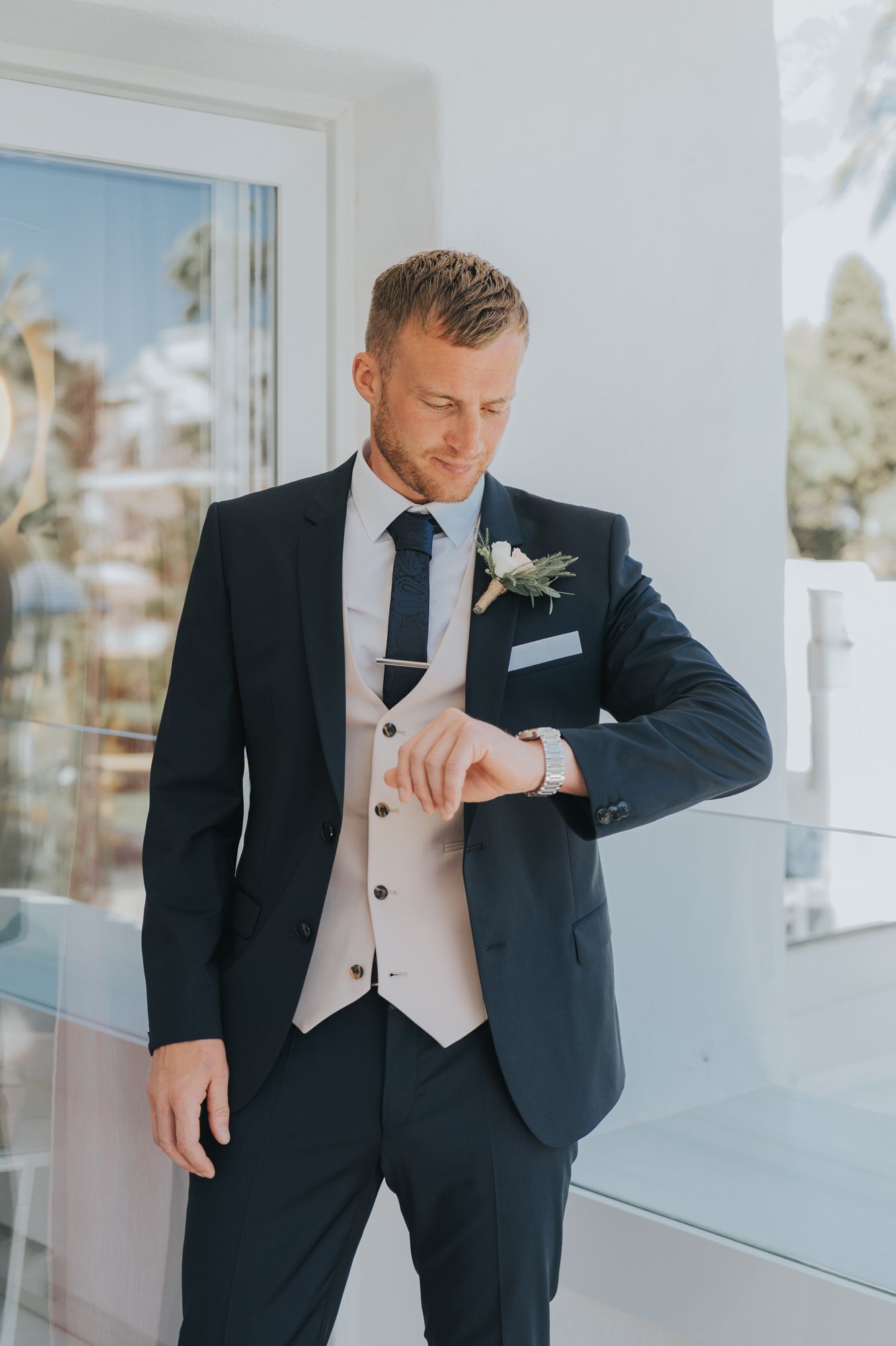 Groom in navy suit with light vest checking time before ceremony.