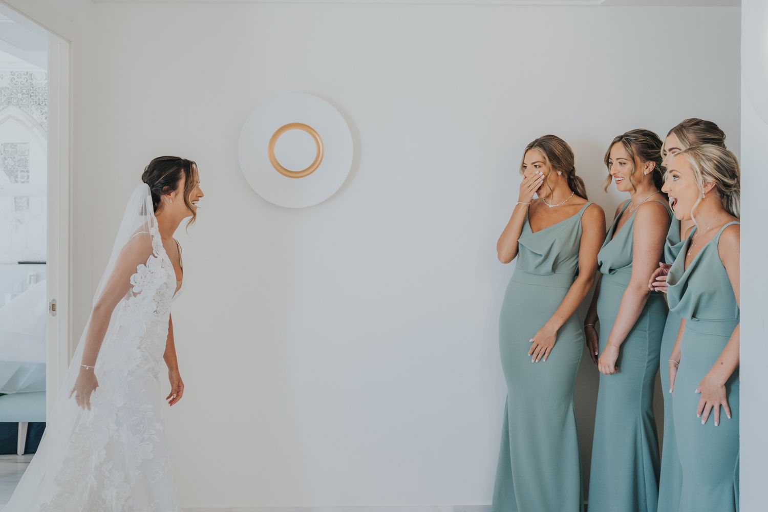 A wedding party reacts with joy as they see the bride in her dress.