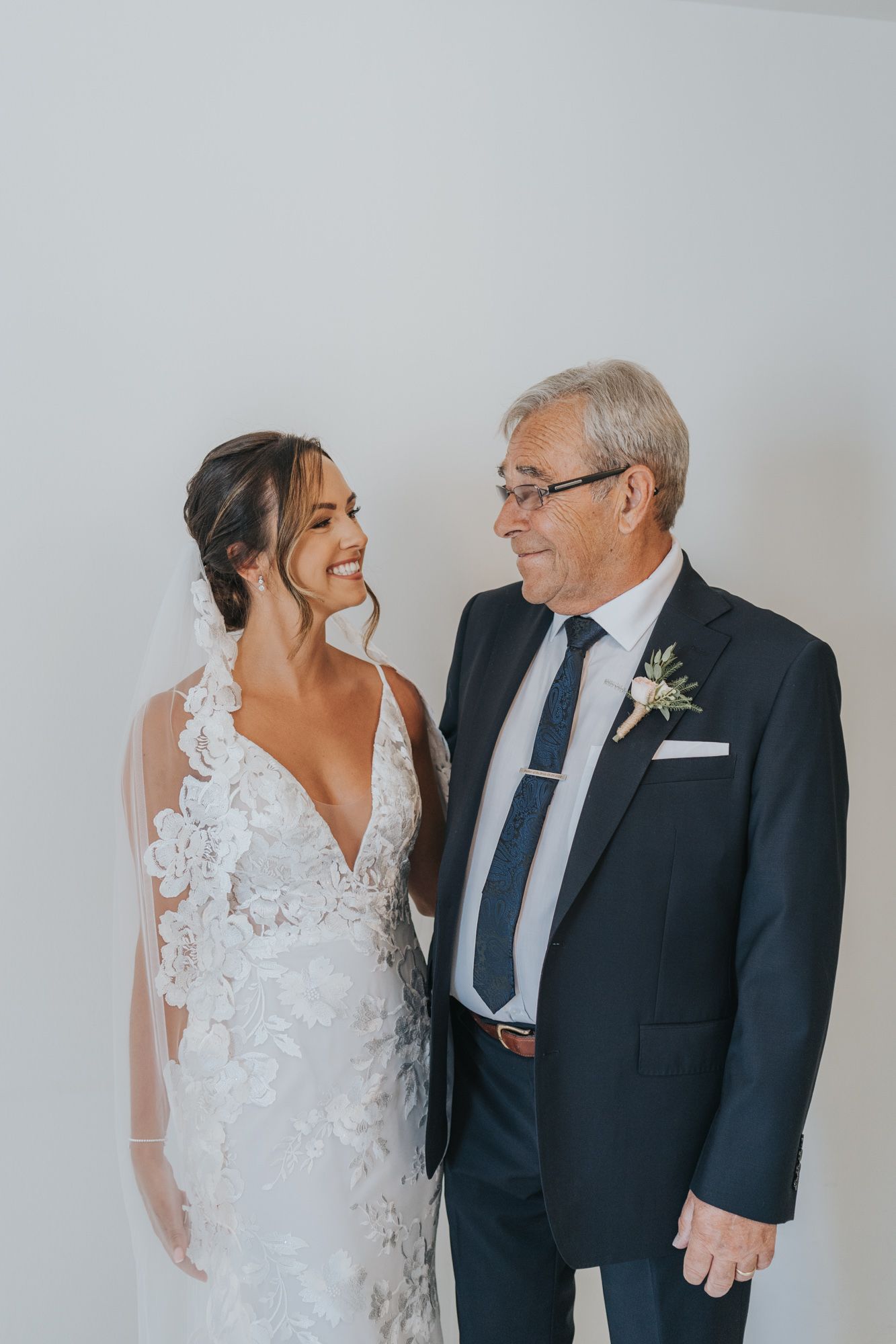 A tender moment between a bride in a lace wedding dress and an older gentleman in a navy suit.