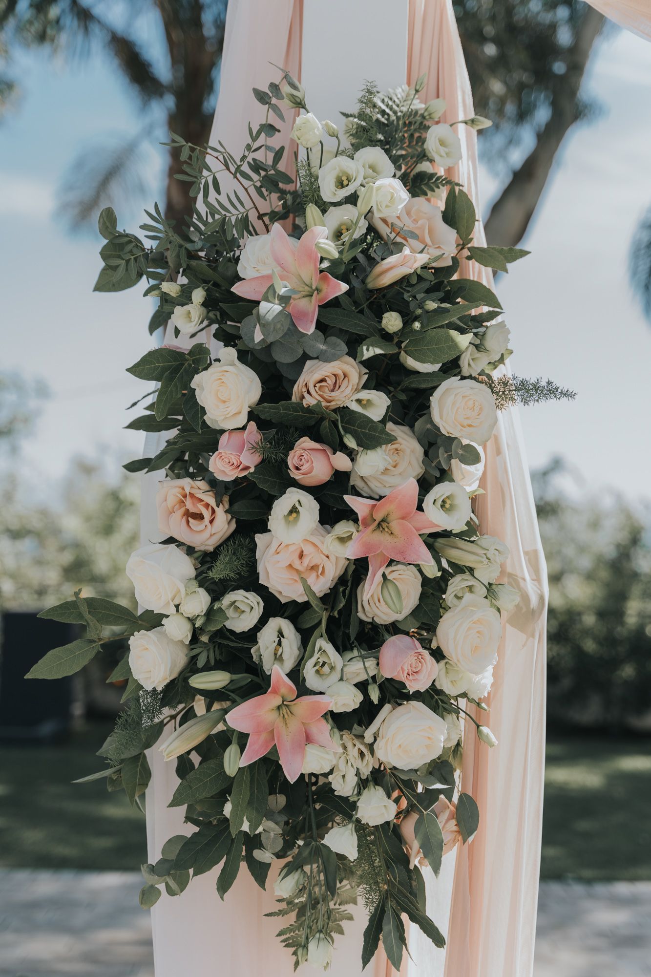 Elegant floral arrangement with pink and white roses and lilies draped on wedding ceremony arch.