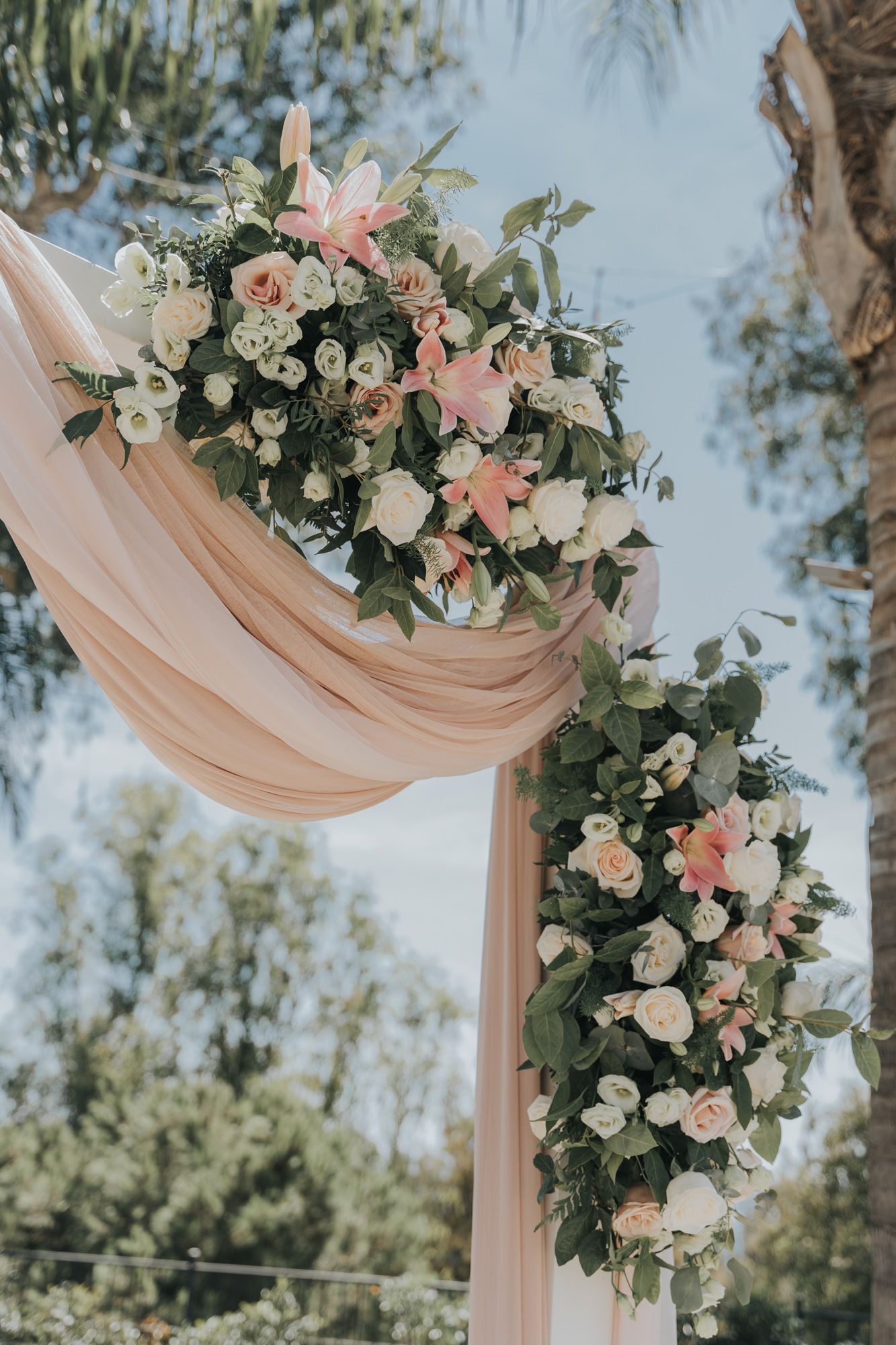 Close-up of blush and white floral arrangement on draped wedding arch.
