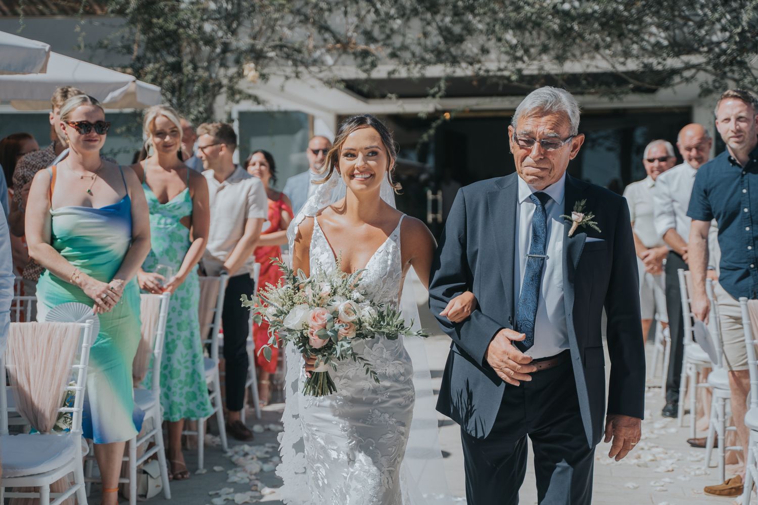 Walking down the aisle during an outdoor wedding ceremony with bridesmaids in turquoise dresses.