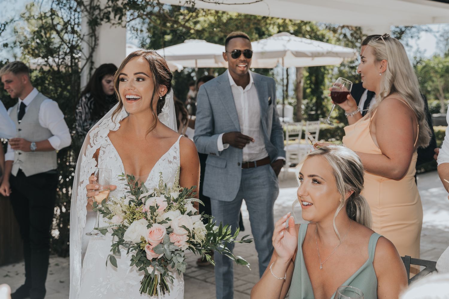 Wedding party members share joyful moments during an outdoor celebration with bridesmaids in peach dresses.