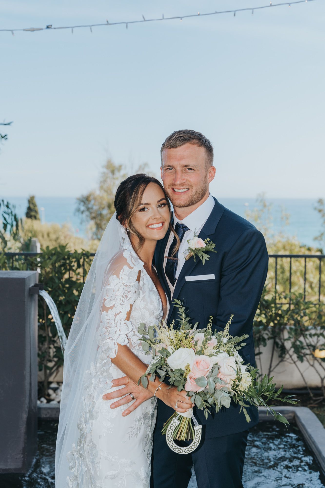 A romantic wedding portrait captured against an ocean backdrop on a bright sunny day.