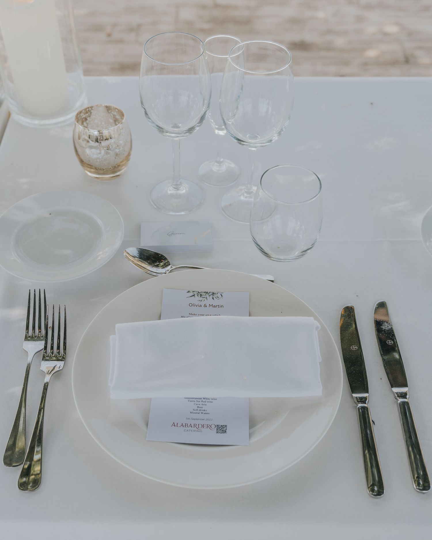 A formal place setting with white dishes, multiple glasses, and silver cutlery on a crisp white tablecloth.