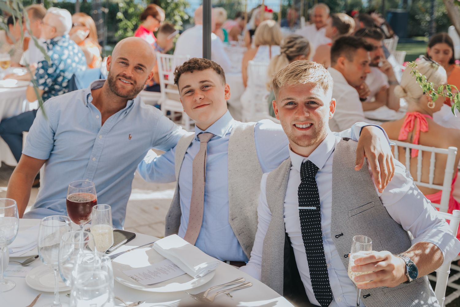 Wedding guests smiling and enjoying themselves at an outdoor reception table.