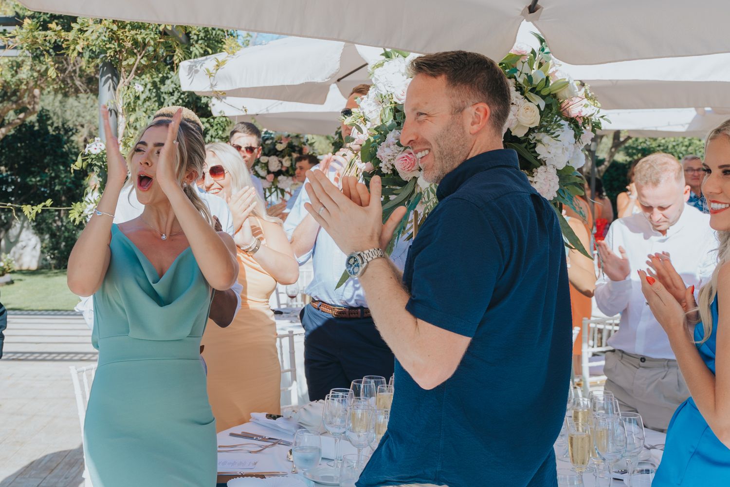 Wedding guests in formal attire celebrate enthusiastically during outdoor reception.