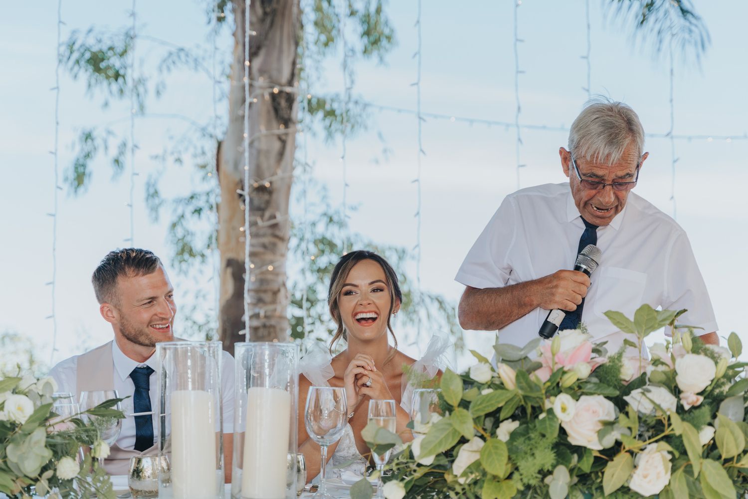 A candid moment during wedding speeches with floral centerpieces and candles on the table.