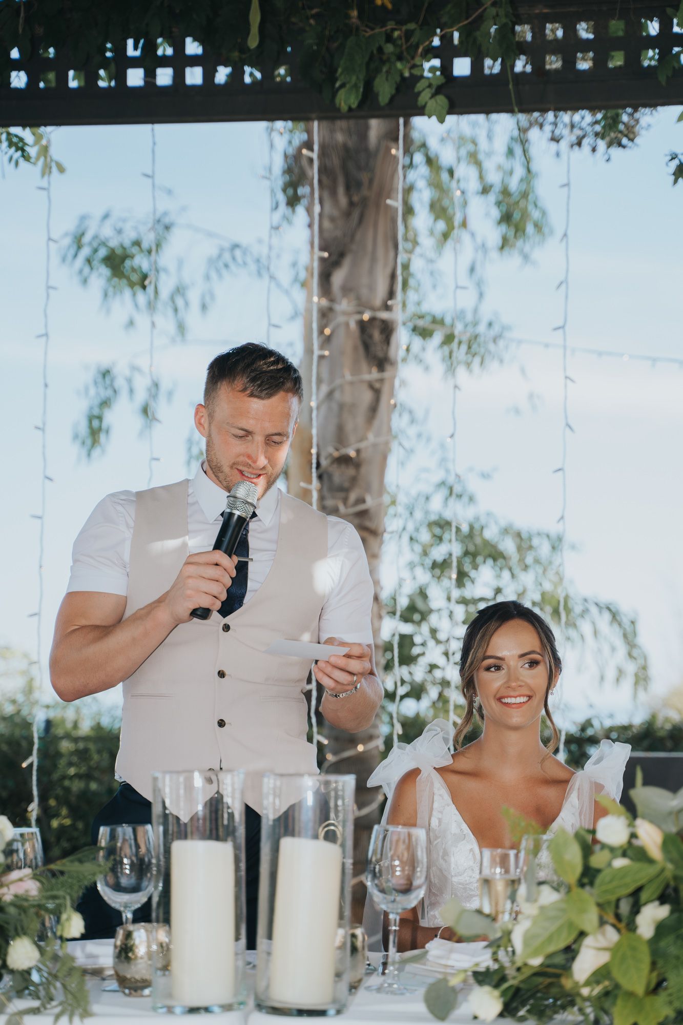 A wedding reception speech moment with elegant table settings and floral arrangements.