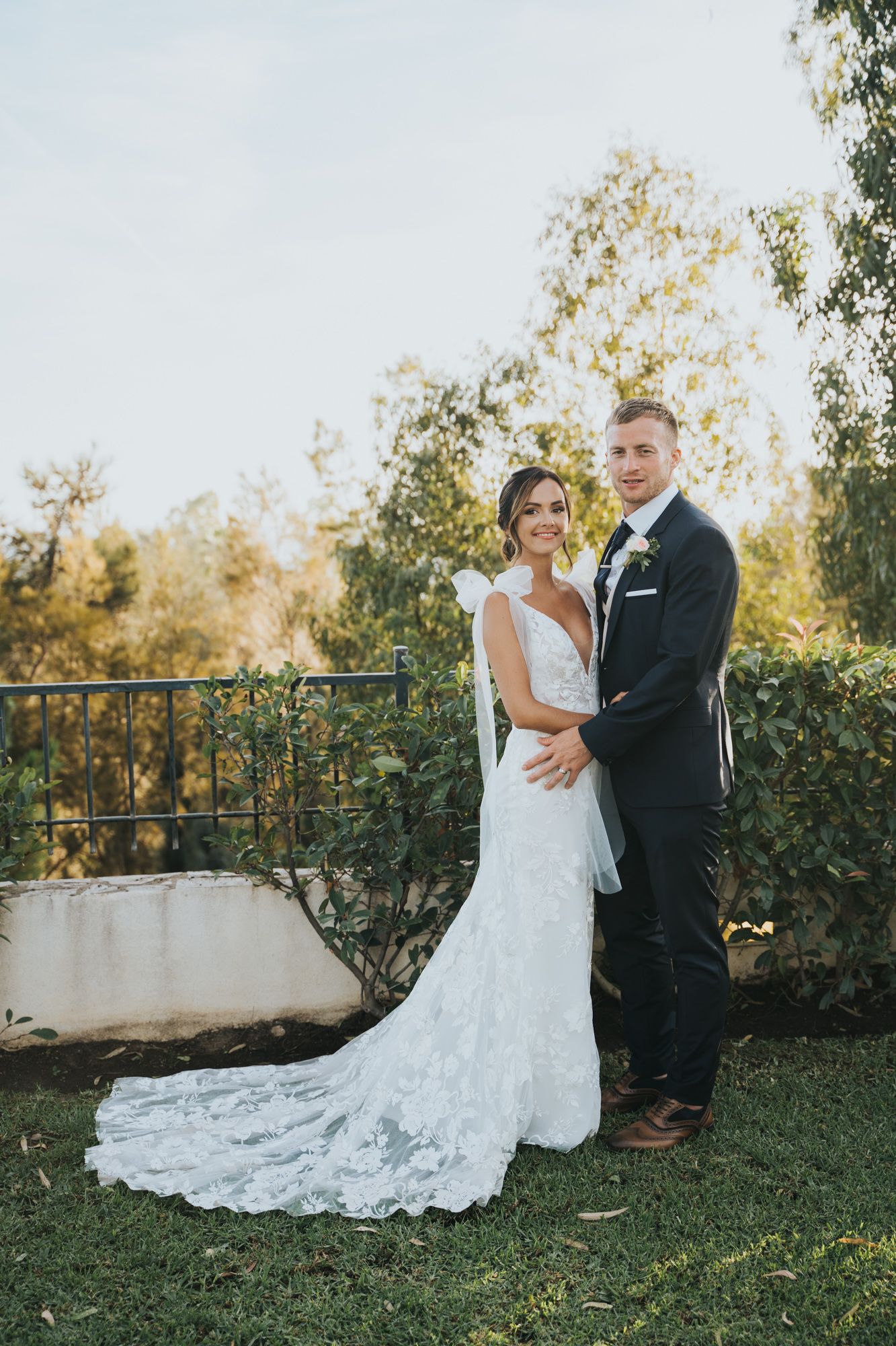 A couple in wedding attire poses for a portrait in a garden setting at sunset.