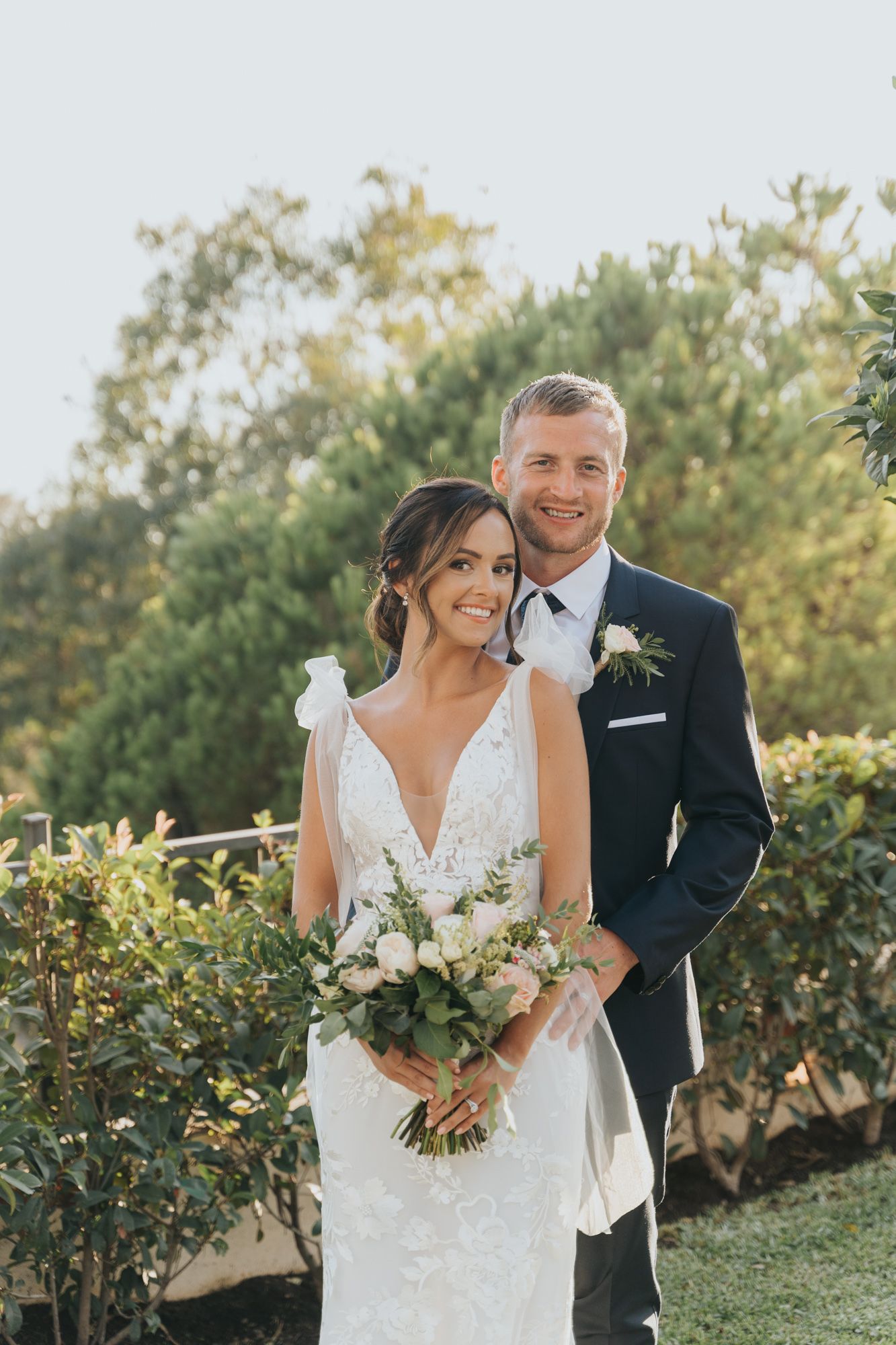 A couple shares a romantic moment in their wedding attire while holding a white floral bouquet.