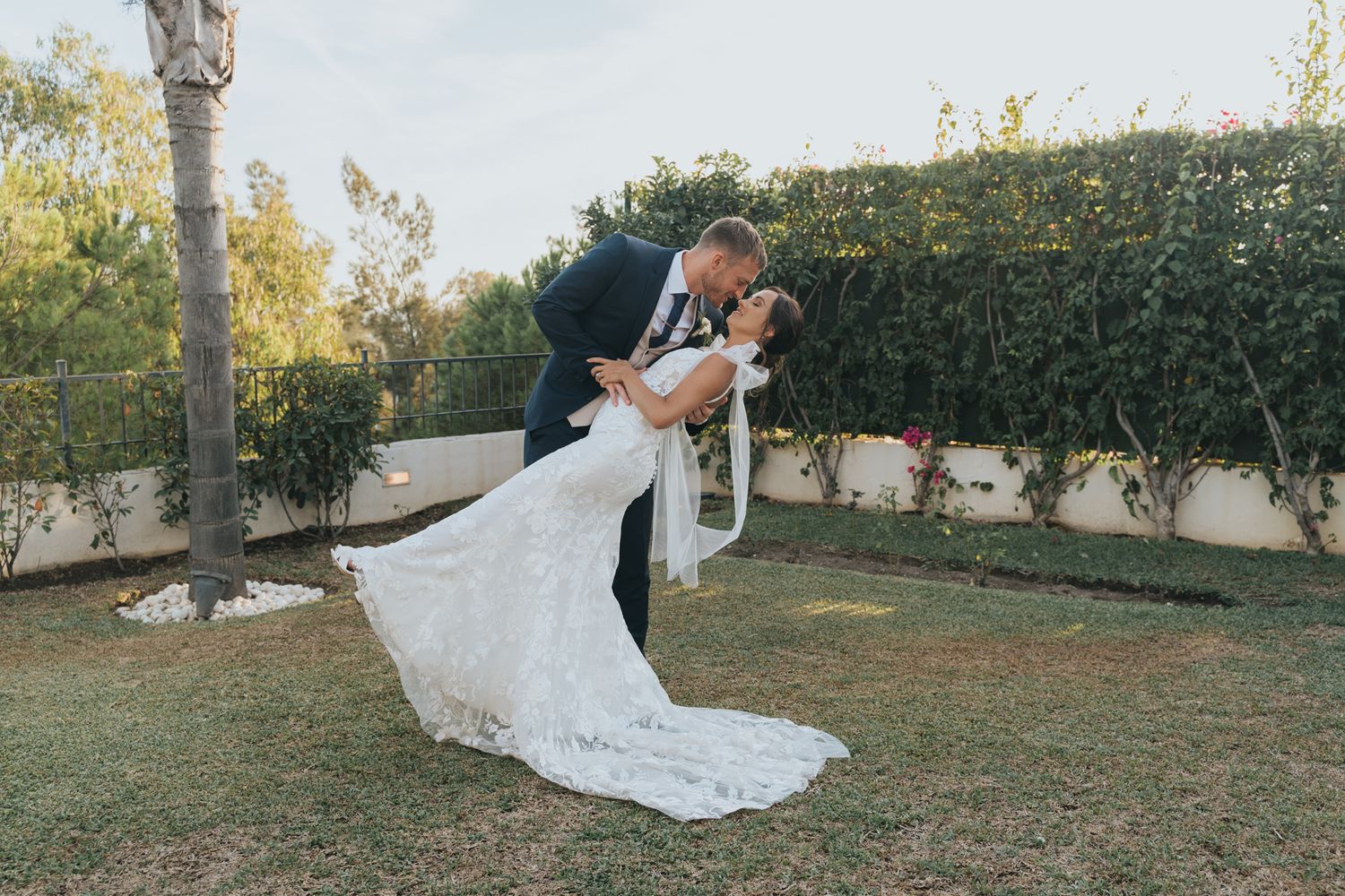 A romantic dip during a garden wedding photo session with a flowing lace gown against a manicured hedge backdrop.