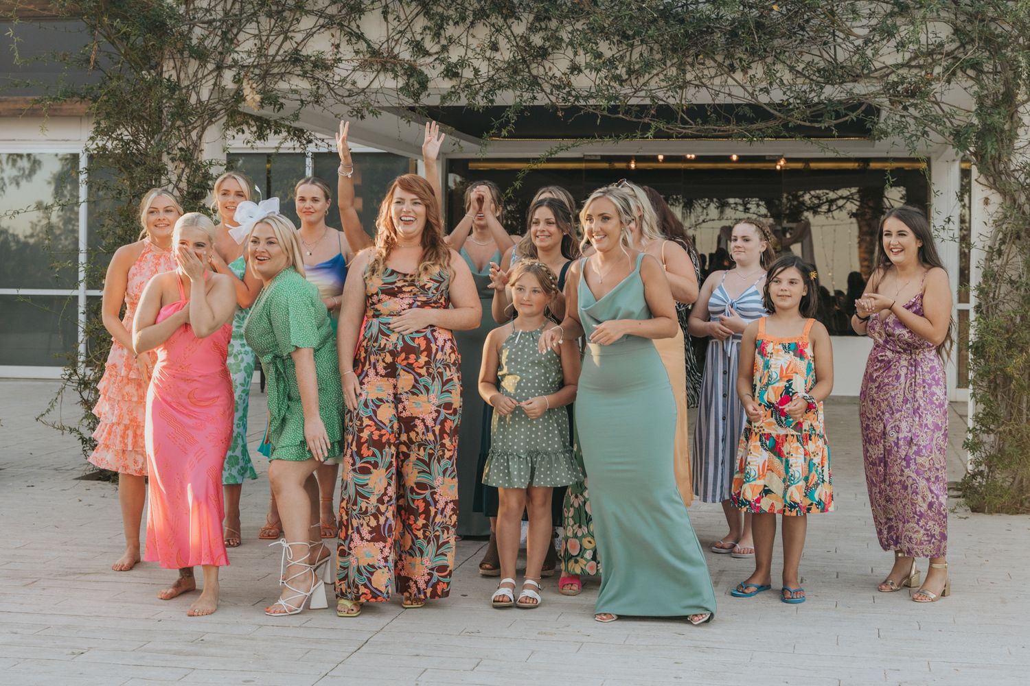 A group of women in colorful floral and solid maxi dresses pose together at an outdoor event.